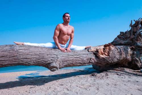 man splits tree yoga beach