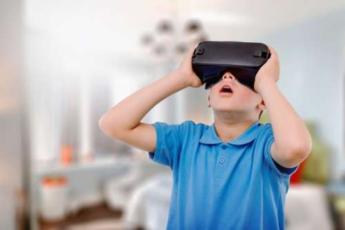 Amazed teen boy wearing virtual reality goggles watching movies or playing video games.