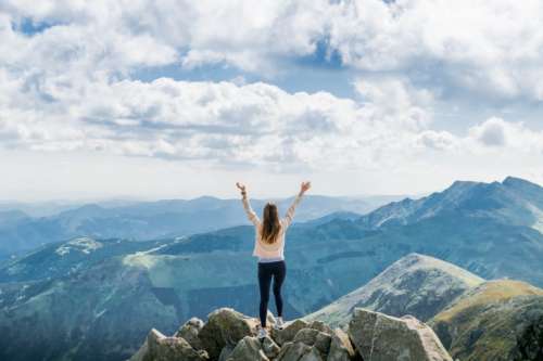 Young successful woman open arms on mountain peak