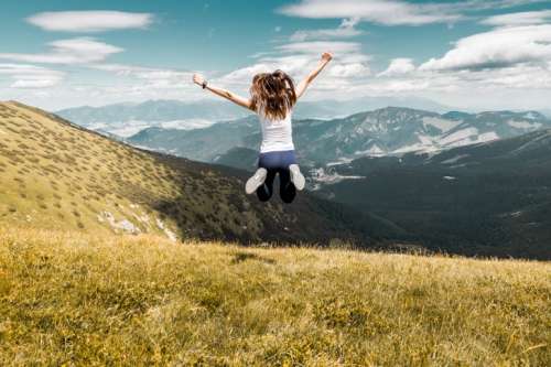 Young woman jumping on top of the summer mountains