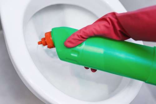 Woman hand with spray bottle cleaning a toilet bowl in a bathroom