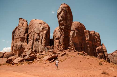 A Man With A Camera Stands Small Against Red Desert Pillars Photo