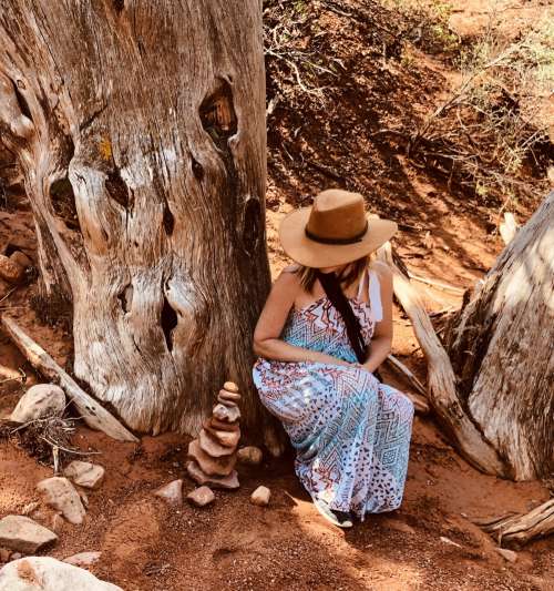 A Woman In Cowboy Hat Crouches By A Tree In The Desert Photo