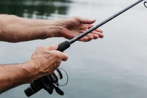 Aged Hands Hold A Fishing Rod Over Still Waters Photo