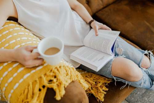 A woman with a cup of coffee reads a book