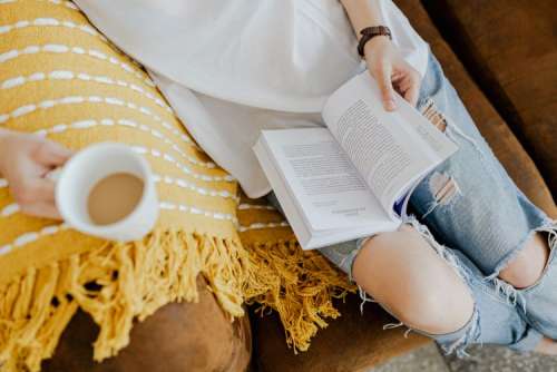 A woman with a cup of coffee reads a book