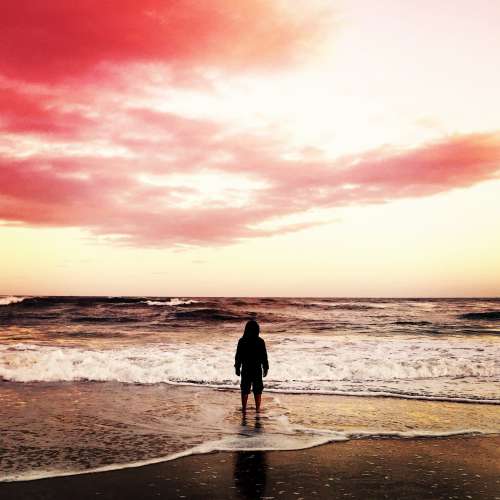 A Figure In A Hoodie On A Beach At The Shoreline Photo