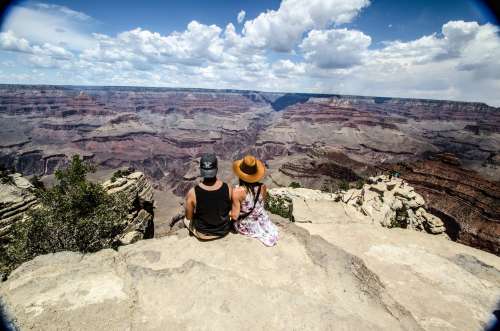 A Young Woman And Man Sit Overlooking A Canyon Photo