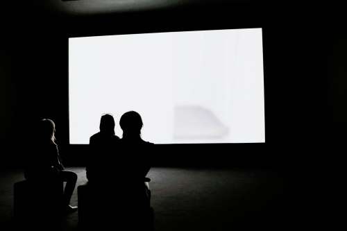 Three Woman Watch A Glowing White Screen In a Dark Room Photo