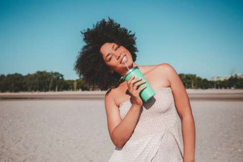 Young Woman Holding Drink Cup With Straw On Sandy Beach Photo