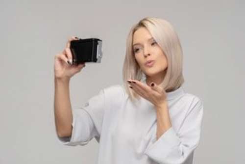 Young Woman Taking A Selfie With An Old Camera And Sending Air Kiss