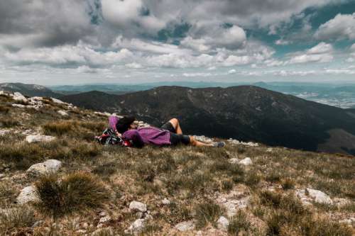 Carefree happy woman lying on green grass meadow on top of mountain