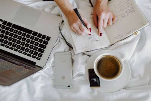 Woman working on a laptop while enjoying a breakfast coffee and chocolate in bed