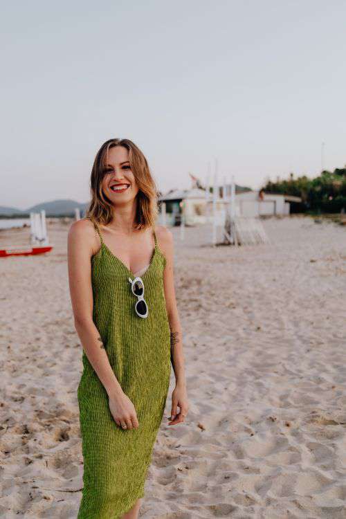 A woman in a green dress on the beach with white sunglasses