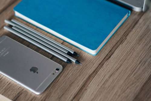Silver iPhone with a blue notebook and pencils
