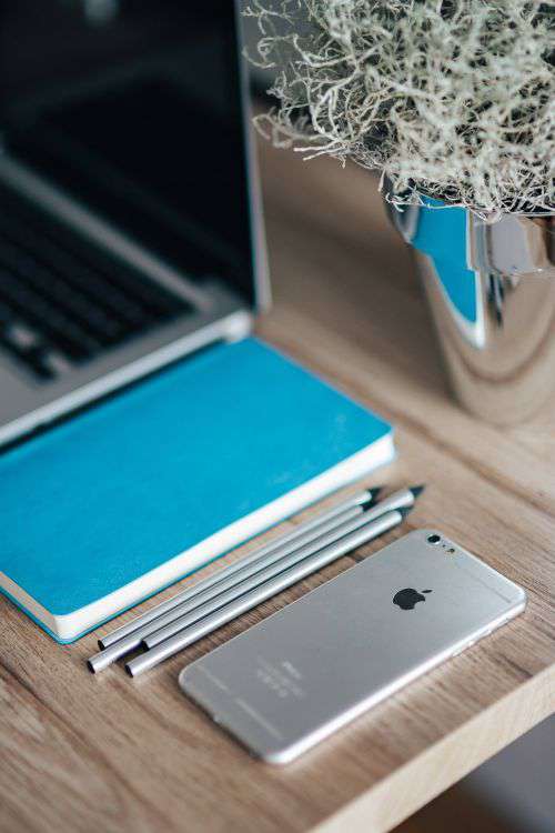 Silver iPhone with a blue notebook and pencils