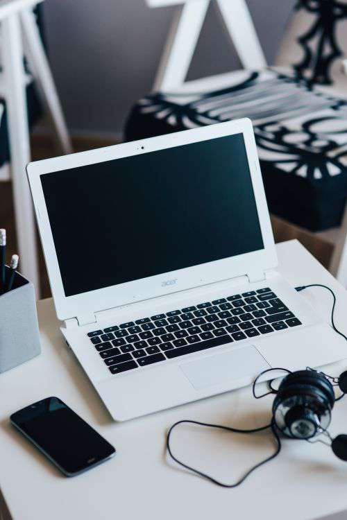 White laptop with smartphone and headphones