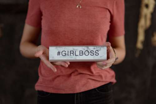 A young woman is holding a Girlboss Desk Sign