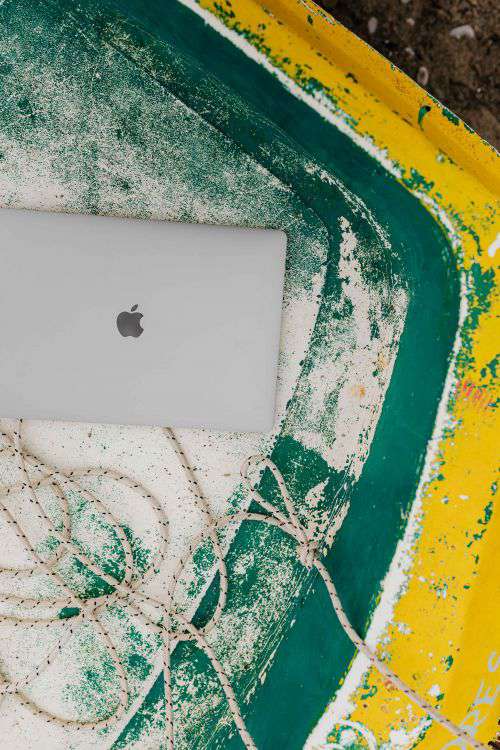 Macbook laptop on a small yellow boat on the beach