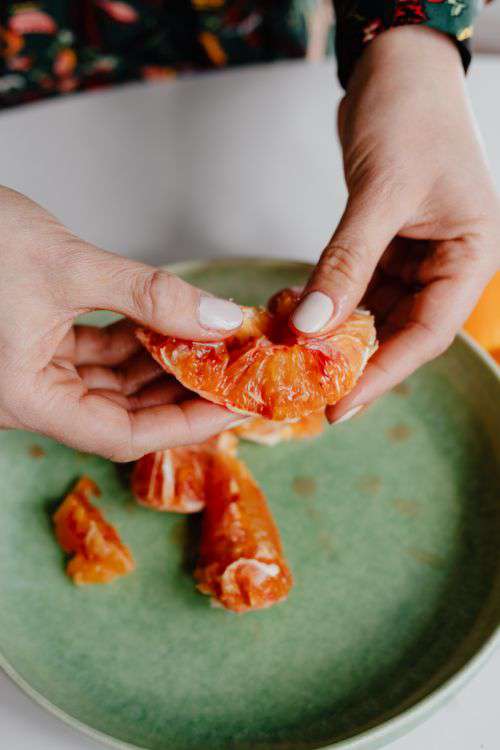 A woman peels an orange on a green plate