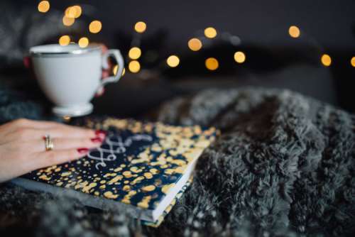Young woman at home reading Hygge book and drinking