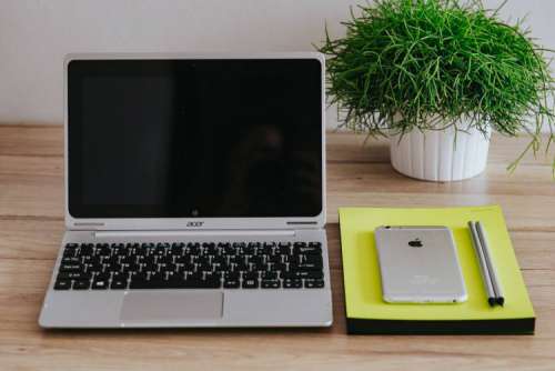 Silver Acer laptop, a white Apple iPhone and a notepad on a wooden desk