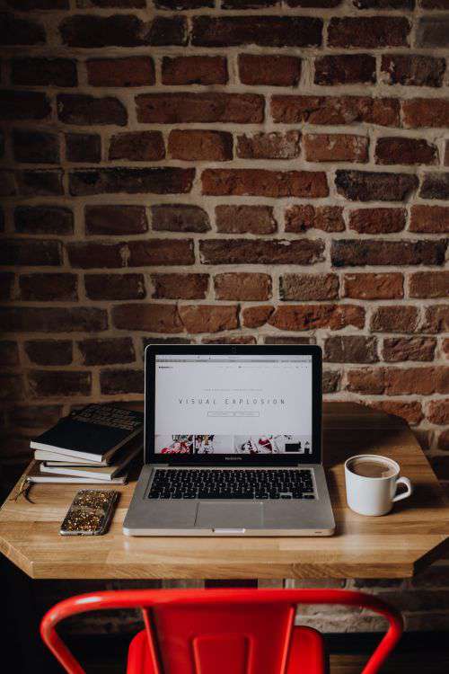 Creatives desk with laptop, camera, journals and books in front of brick wall