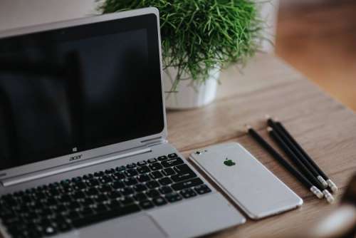 Silver Acer laptop on a wooden desk with a green plant, pencils and an Apple iPhone