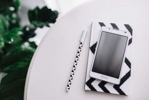 Black-and-white notebook and a white smartphone with various items