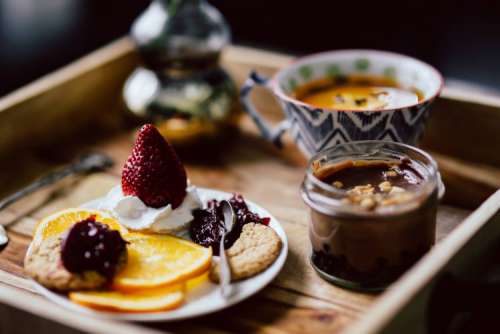 Room service tray at hotel for breakfast: cookies, jam, chocolate mousse, orange fruit, tea