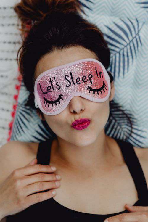 Joyful girl relaxing in bedroom - top view of brunette women in pink sleeping mask