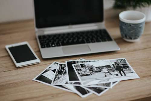 Black-and-white photos with a silver laptop, a smartphone, car keys, pencils and a camera