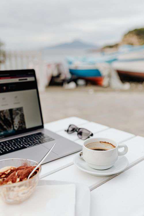 Working with a laptop by the sea. Cup of coffee and delicious tiramisu, Marina di Puolo, Italy