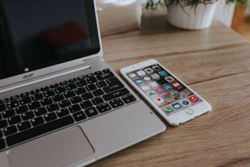 Silver Acer laptop, a white Apple iPhone and a notepad on a wooden desk