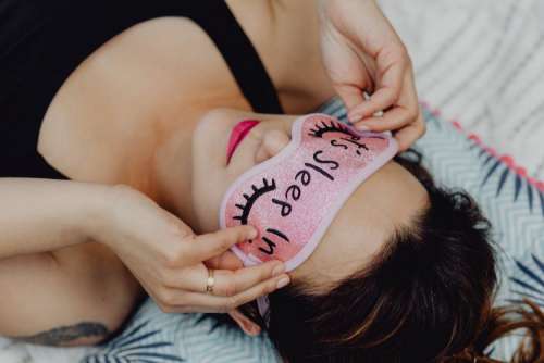 Joyful girl relaxing in bedroom - top view of brunette women in pink sleeping mask