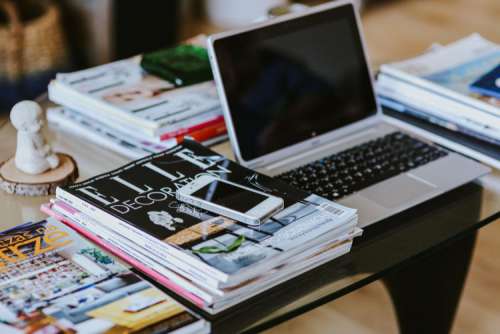 Laptop, a smartphone, magazines and cups of coffee on a table