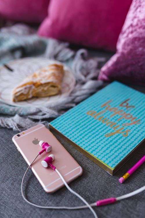 Blue notebook with a pink iPhone, headphones and a sweet bun