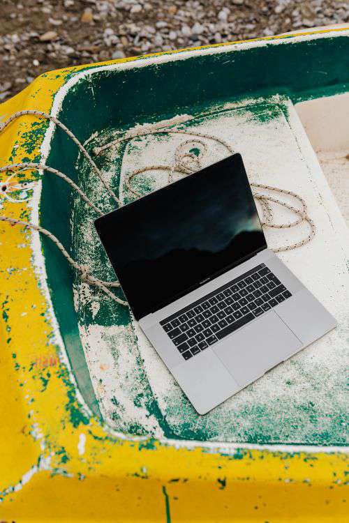 Macbook laptop on a small yellow boat on the beach