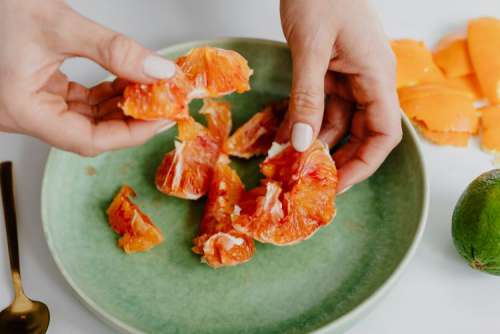A woman peels an orange on a green plate