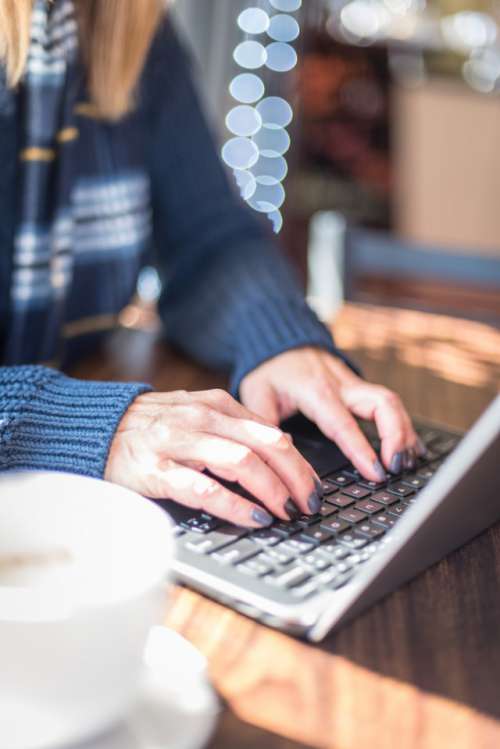 Woman in sweater typing on laptop keyboard at coffee shop in winter