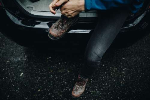 A man, wearing a wedding ring, ties his muddy boots while sitting in the back of a black car