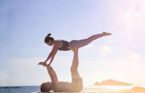 A couple doing high level of yoga posture supporting in each other with harmony on the beach in the sunny day. 