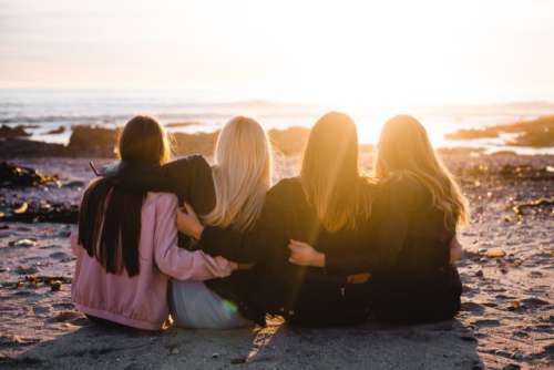Girls sitting on beach watching sunset 