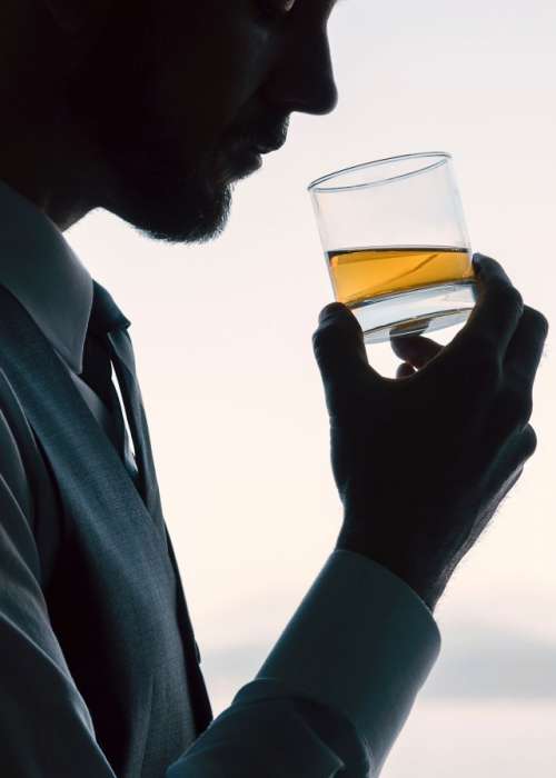 Professional businessman drinking a neat whiskey alcoholic drink silhouetted by bright window