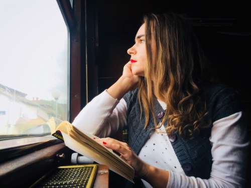 Woman in train sitting next to the window and looking outside with a book in her hand
