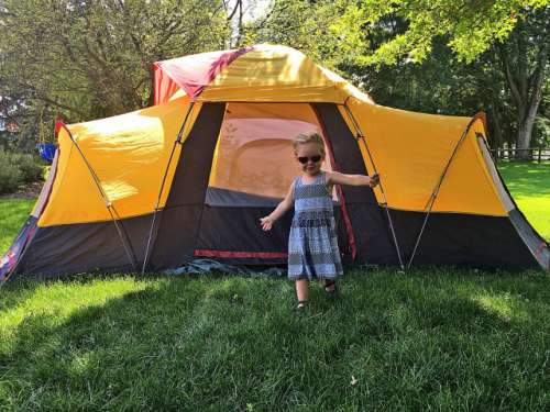 Toddler girl standing in front of a camping tent in summer.