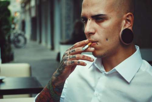 Alternative tattoed boy model with cigarette and white formal shirt. Bokeh background.