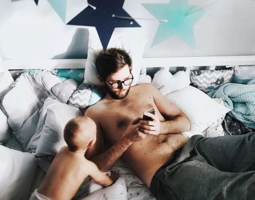 Daddy, using mobile laying with son on the bed in kids room
