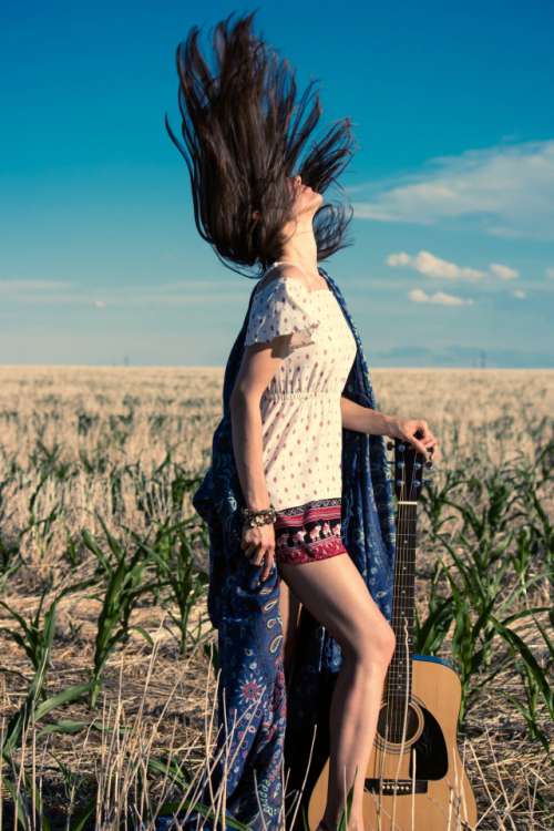 Hippie girl in dress with guitar on the field