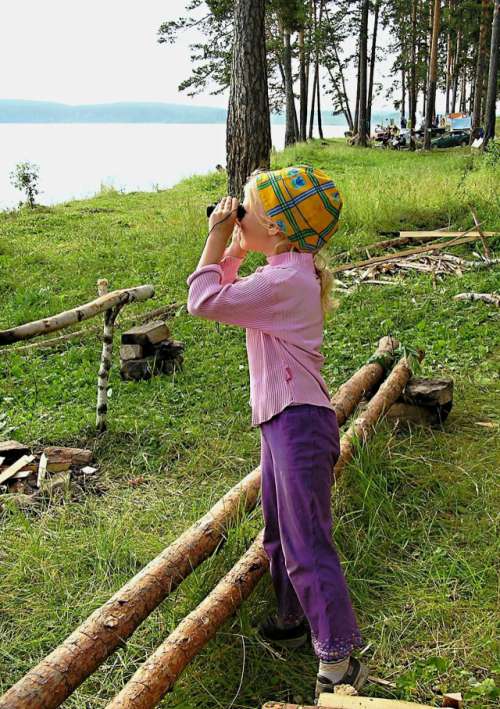 Little girl looking through binoculars at lake